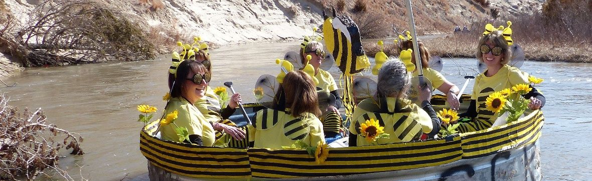 People dressed as bees in yellow and black striped costumes ride a round, decorated boat down a river.