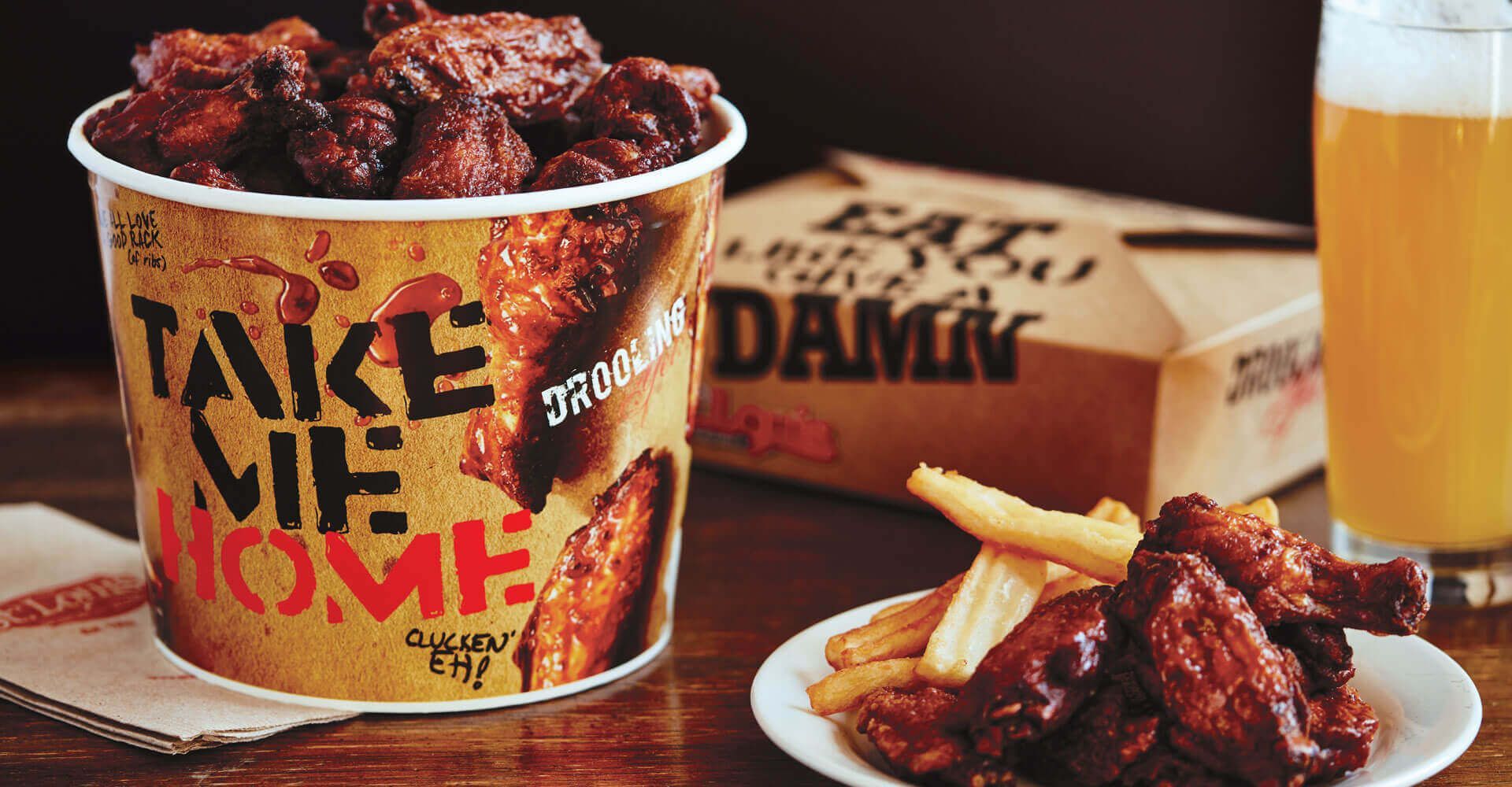 A bucket of chicken wings and a plate of french fries on a table.