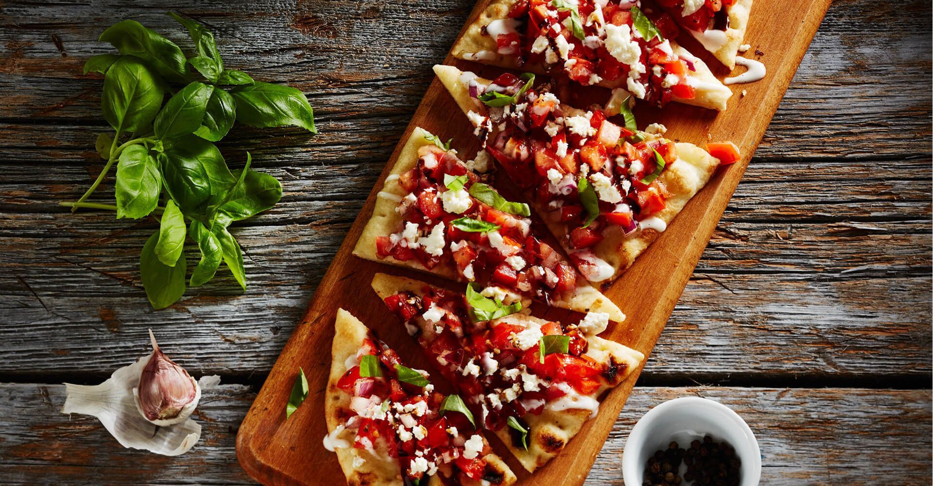 A wooden cutting board topped with slices of pizza on a wooden table.