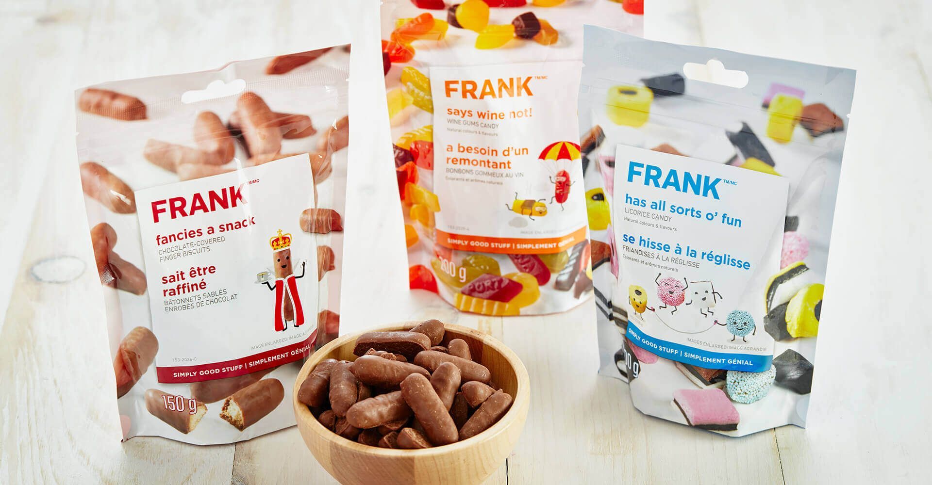 Three bags of frank candy are sitting on a table next to a bowl of candy.