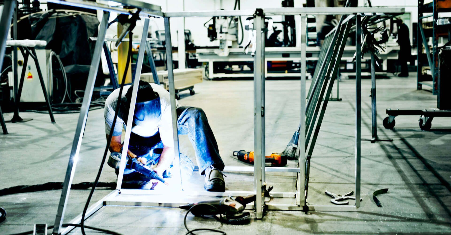 A man is welding a metal structure in a factory.