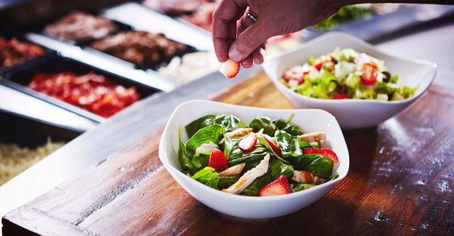 A person is adding strawberries to a salad in a bowl.