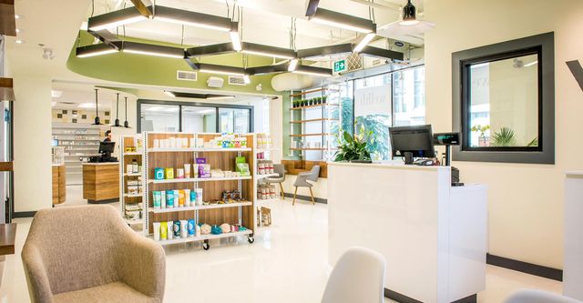 A pharmacy with a reception desk , chairs , shelves and a computer.