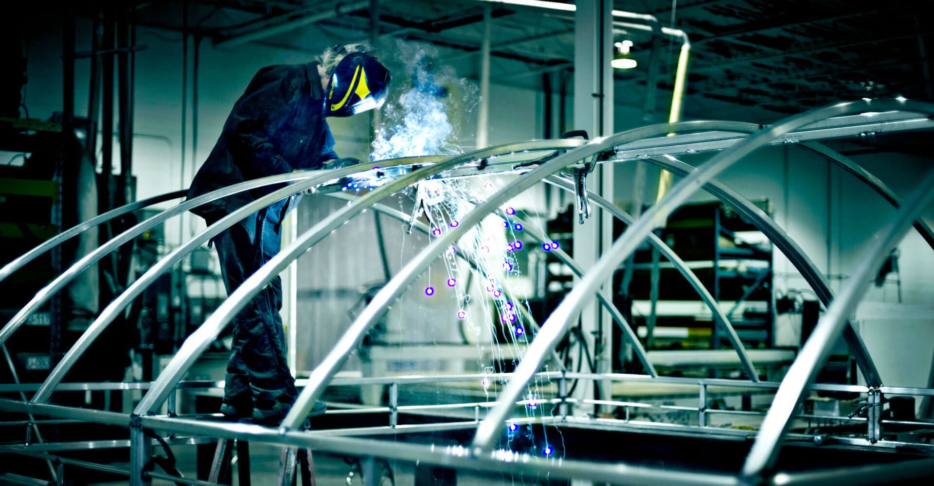 A man is welding a metal structure in a factory.