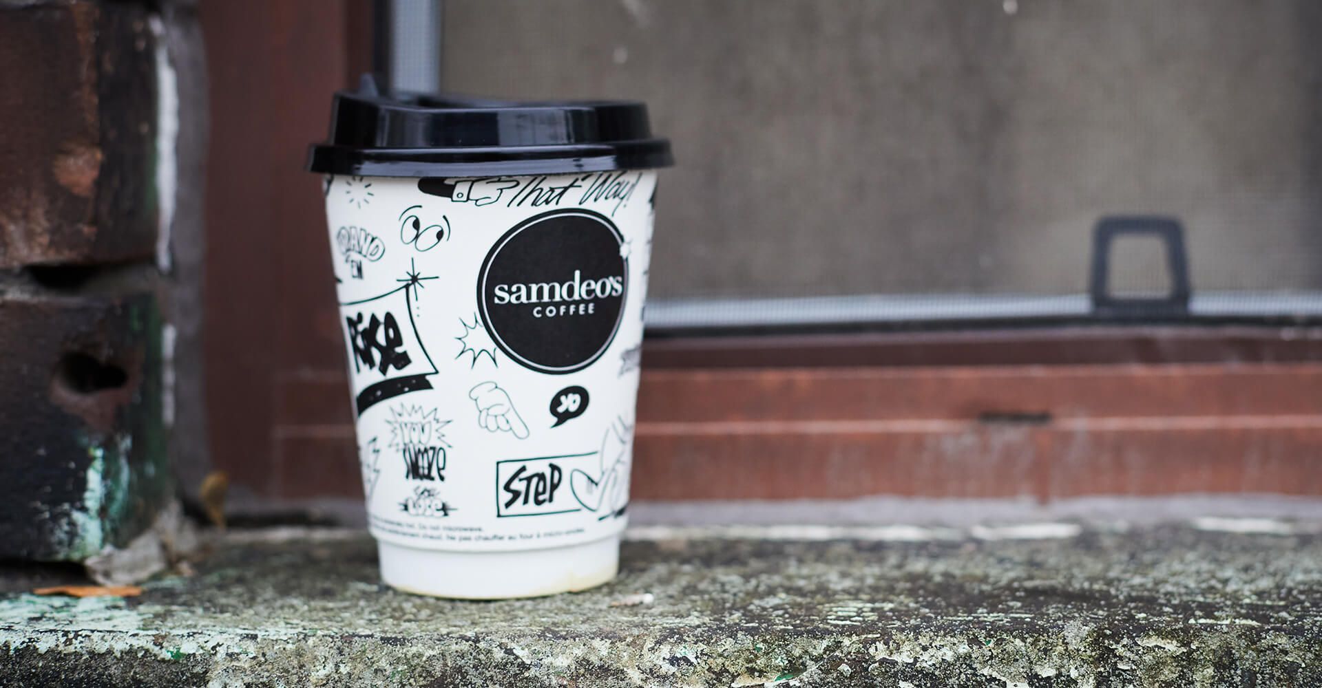 A cup of coffee is sitting on a sidewalk next to a window.