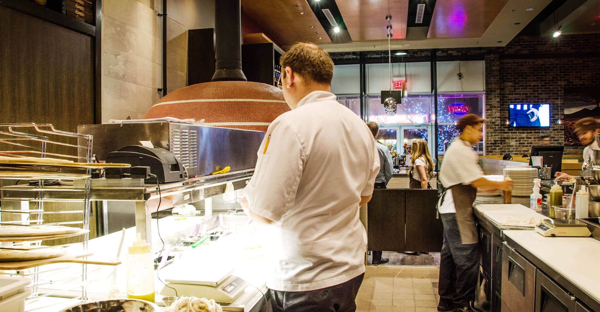 A man in a white chef 's jacket is standing in a restaurant kitchen.
