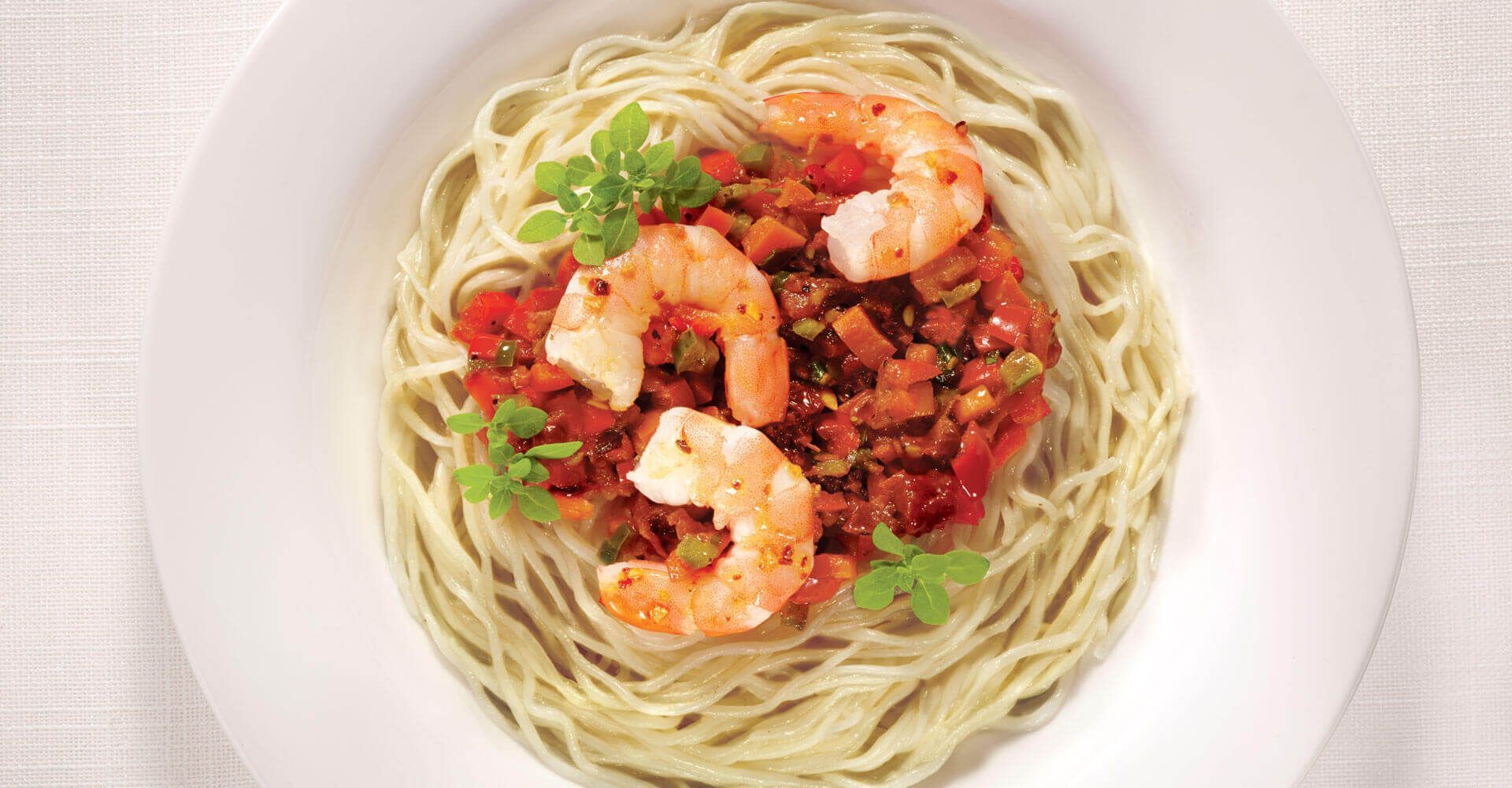 A white plate topped with noodles and shrimp on a table.