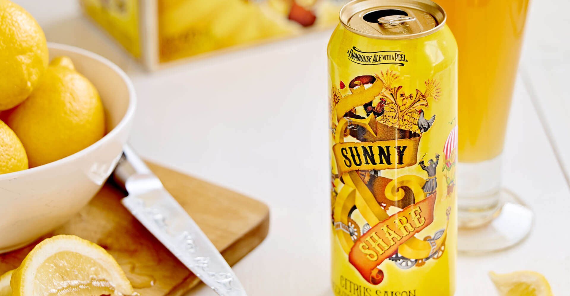 A can of beer is sitting on a table next to a bowl of lemons.