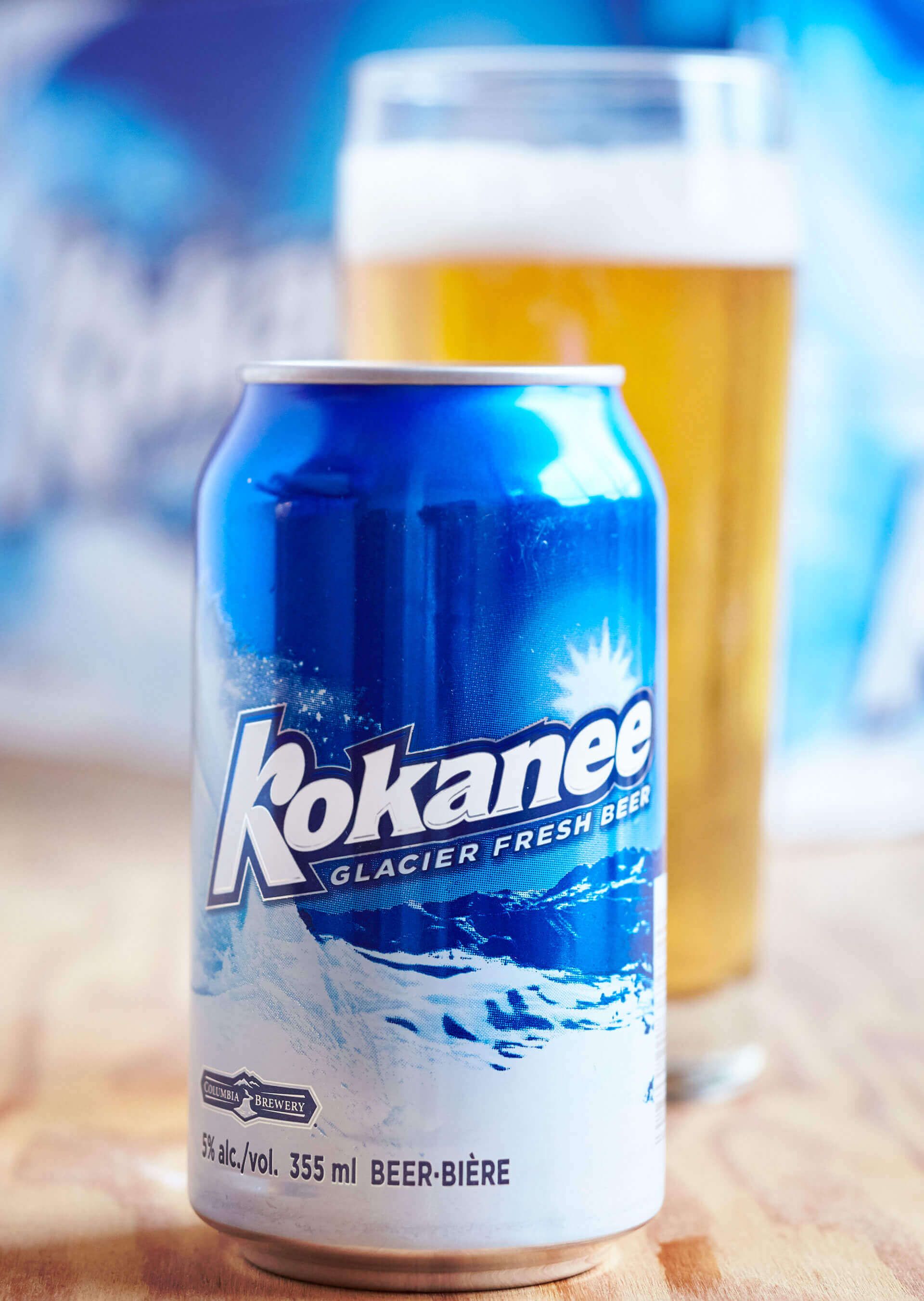 A can of kokanee beer is sitting on a wooden table next to a glass of beer.