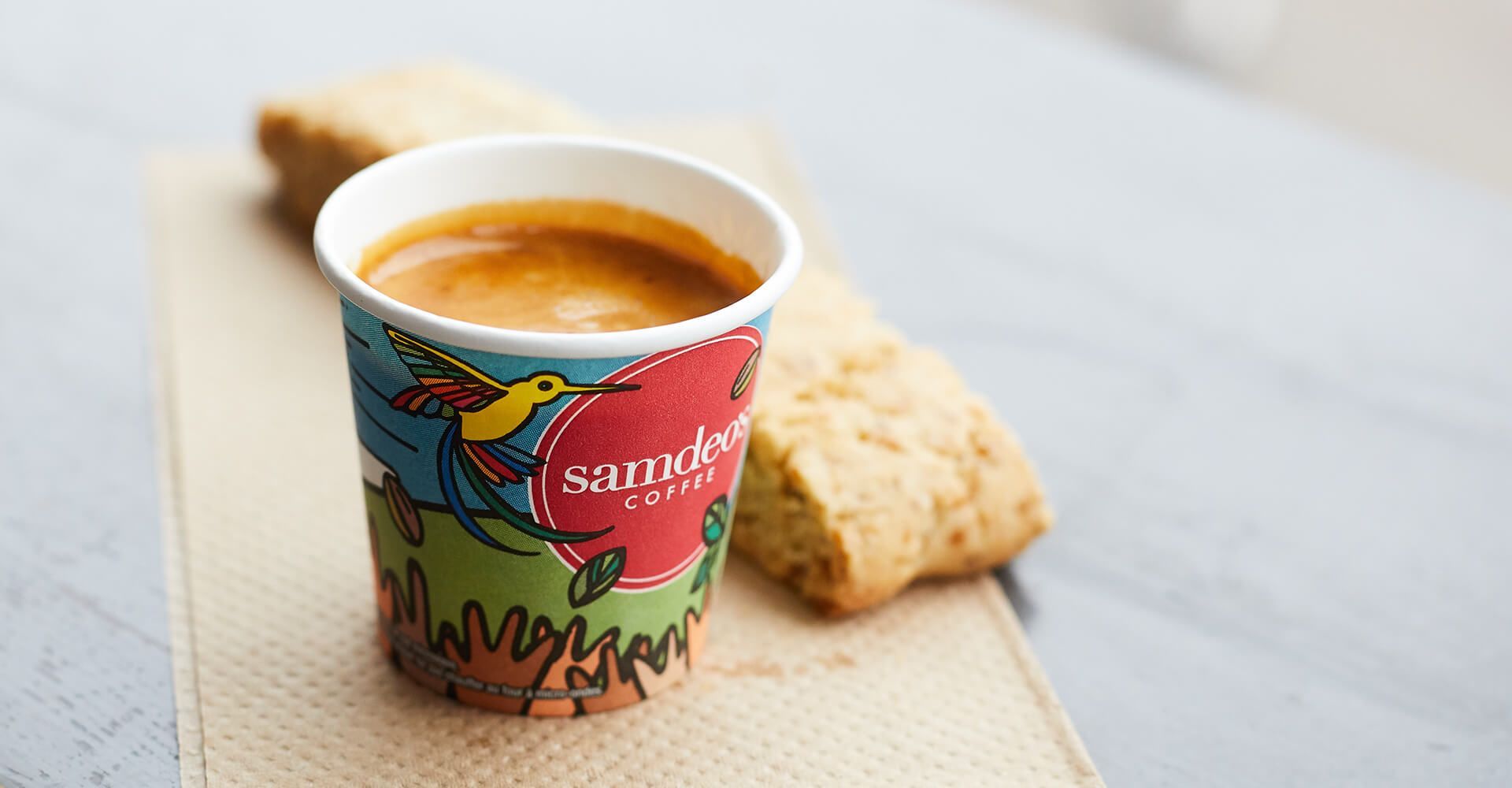 A cup of coffee is sitting on a table next to a piece of bread.