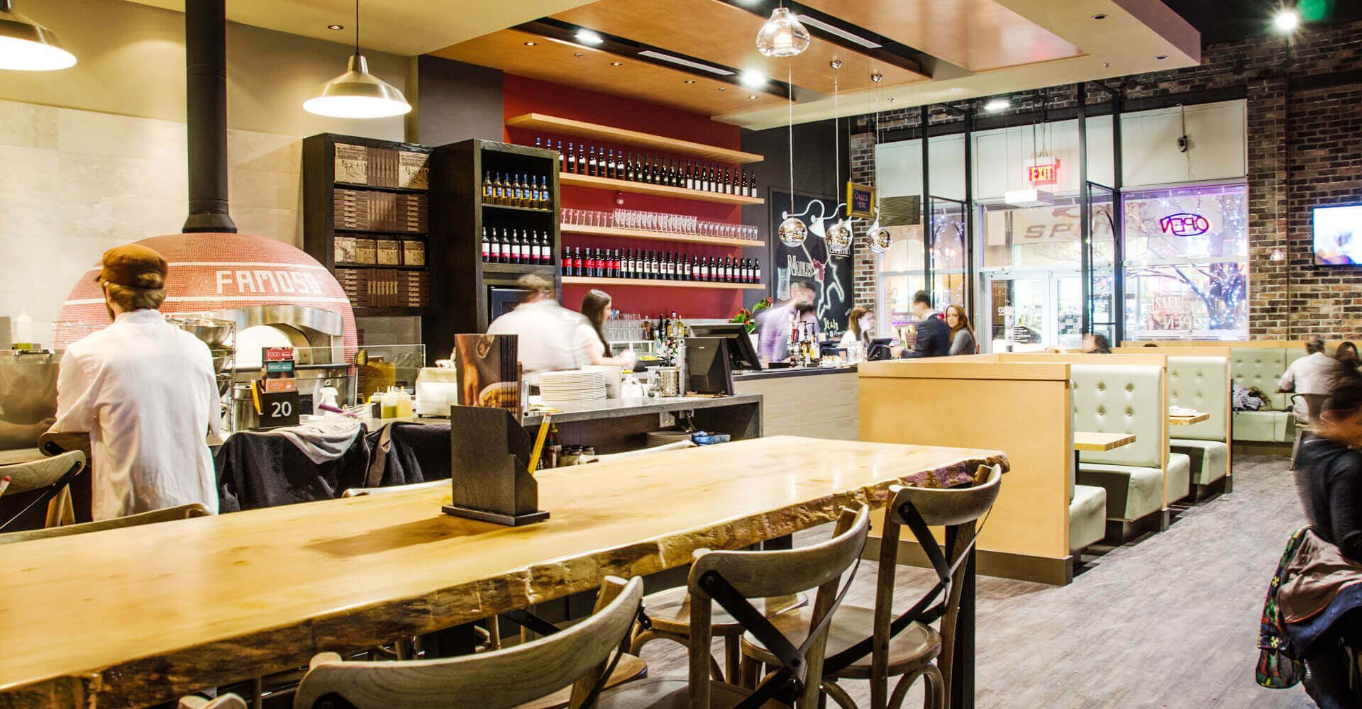 A restaurant with tables and chairs and a pizza oven.