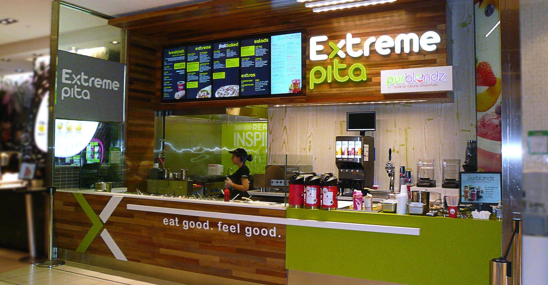 A woman stands behind a counter at an extreme pita restaurant