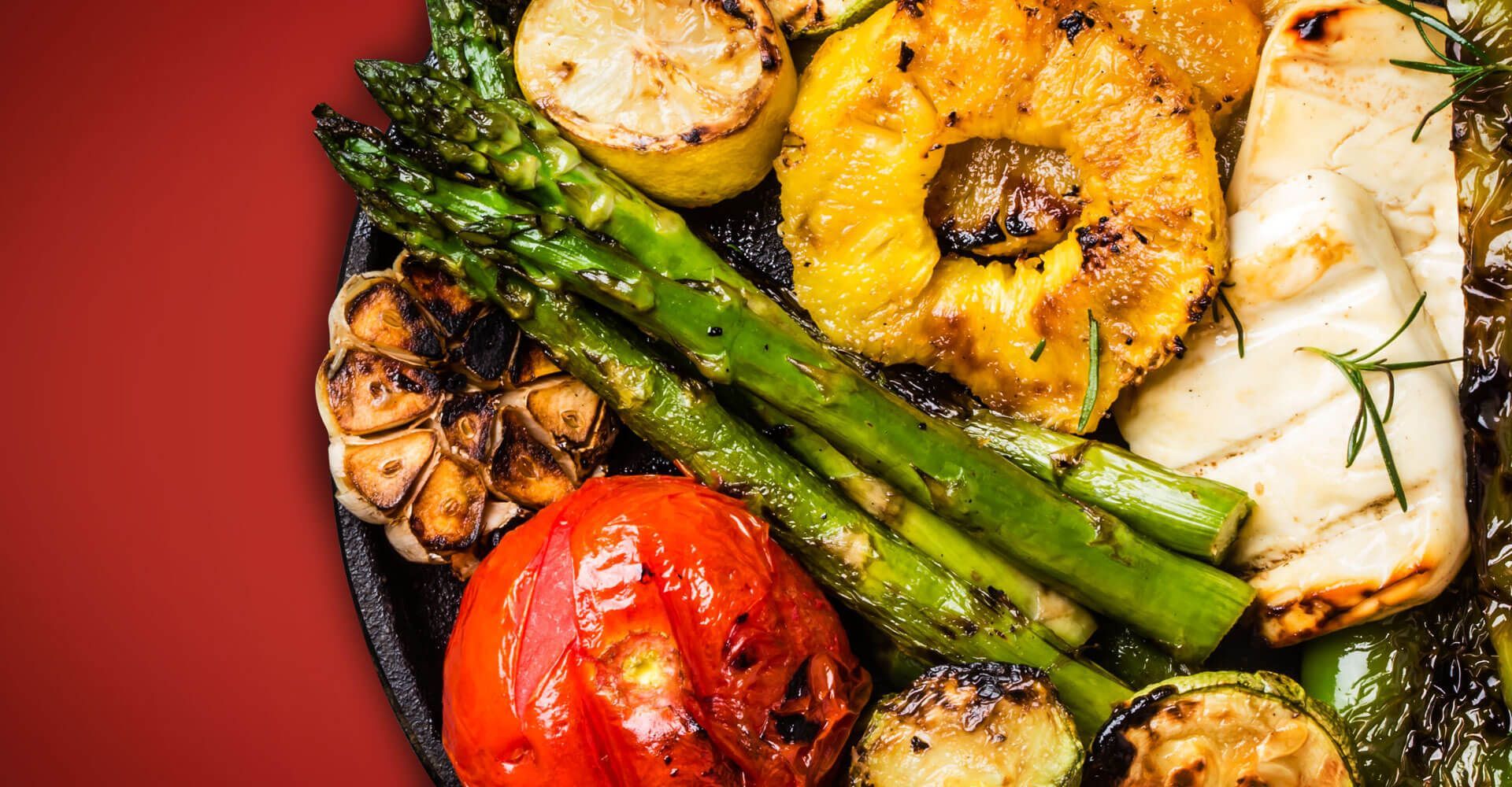 A close up of a plate of grilled vegetables on a red background.