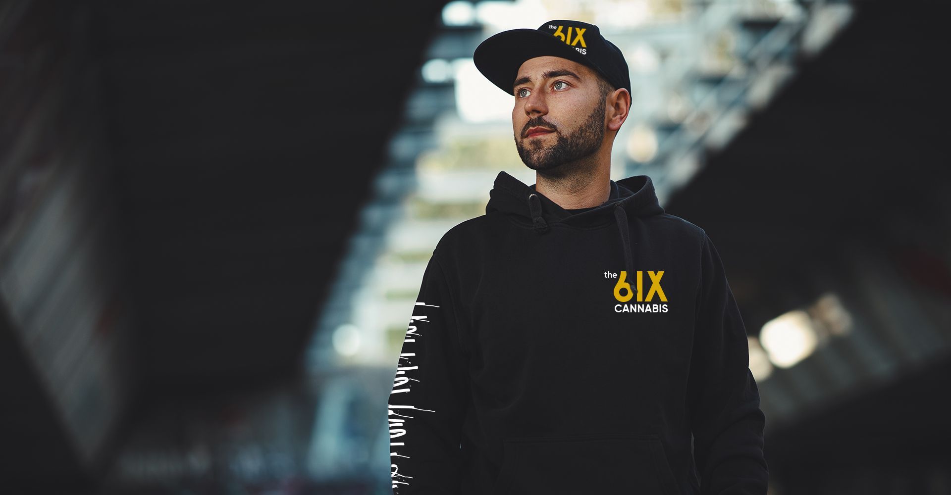 A man wearing a hat and a black hoodie is standing in front of a building.
