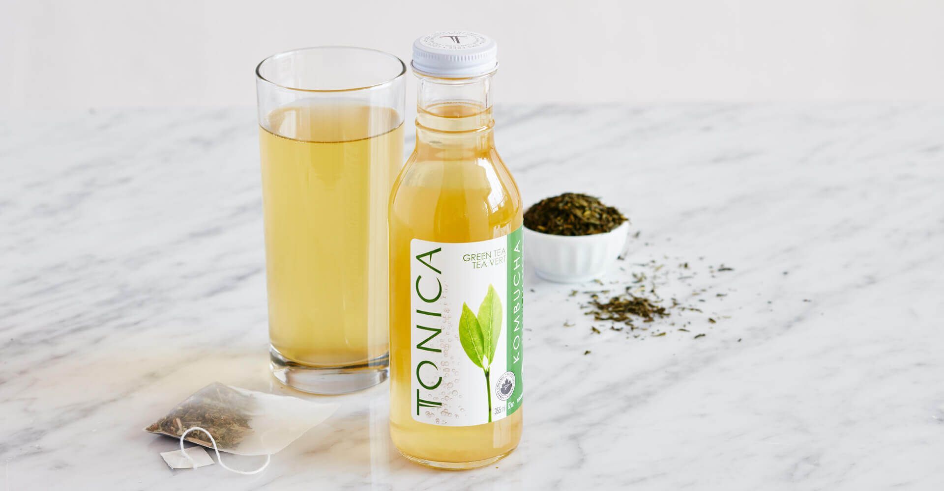 A bottle of tonic tea next to a glass of tea on a table.