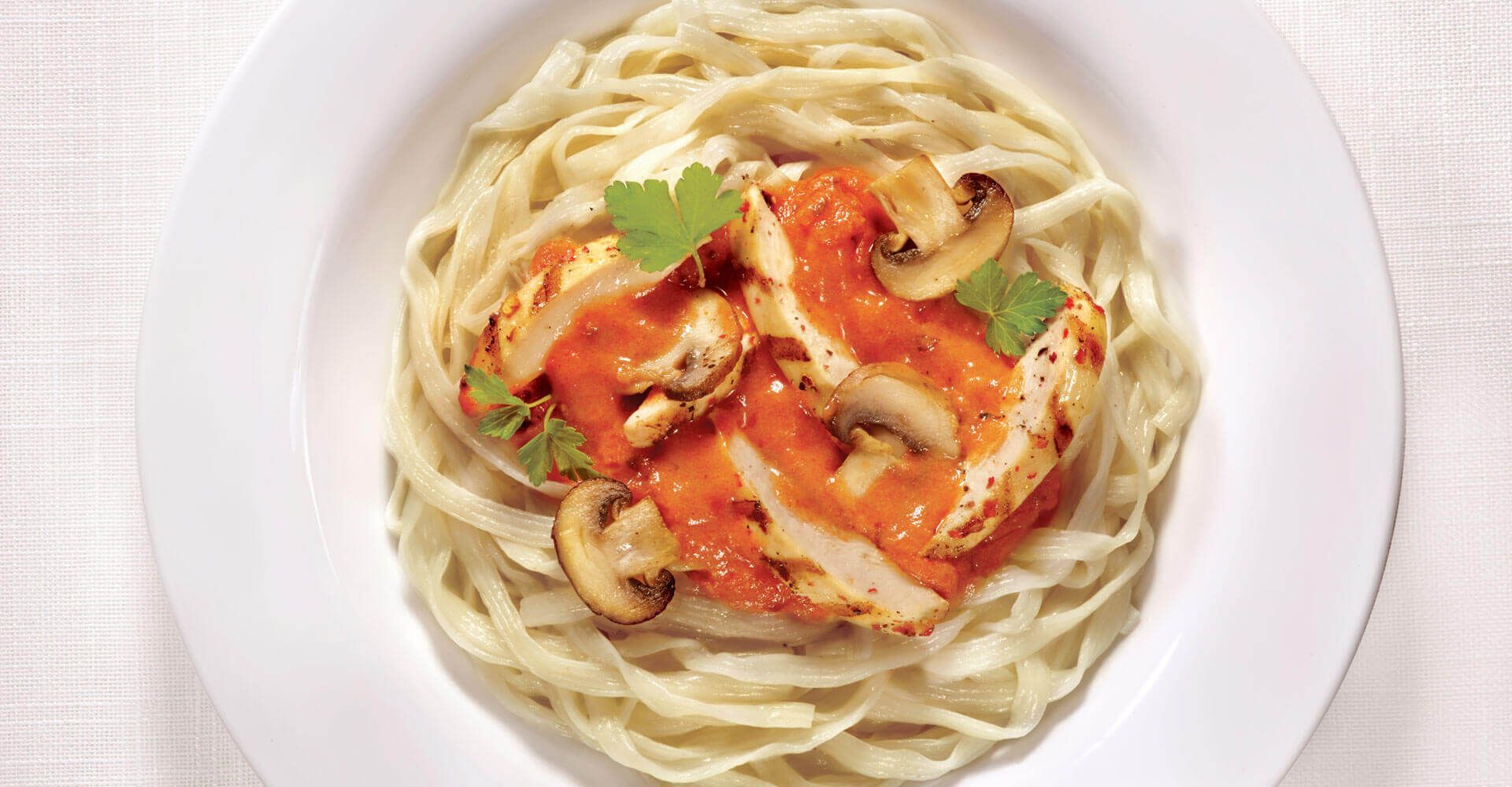 A white plate topped with noodles , mushrooms and tomato sauce.