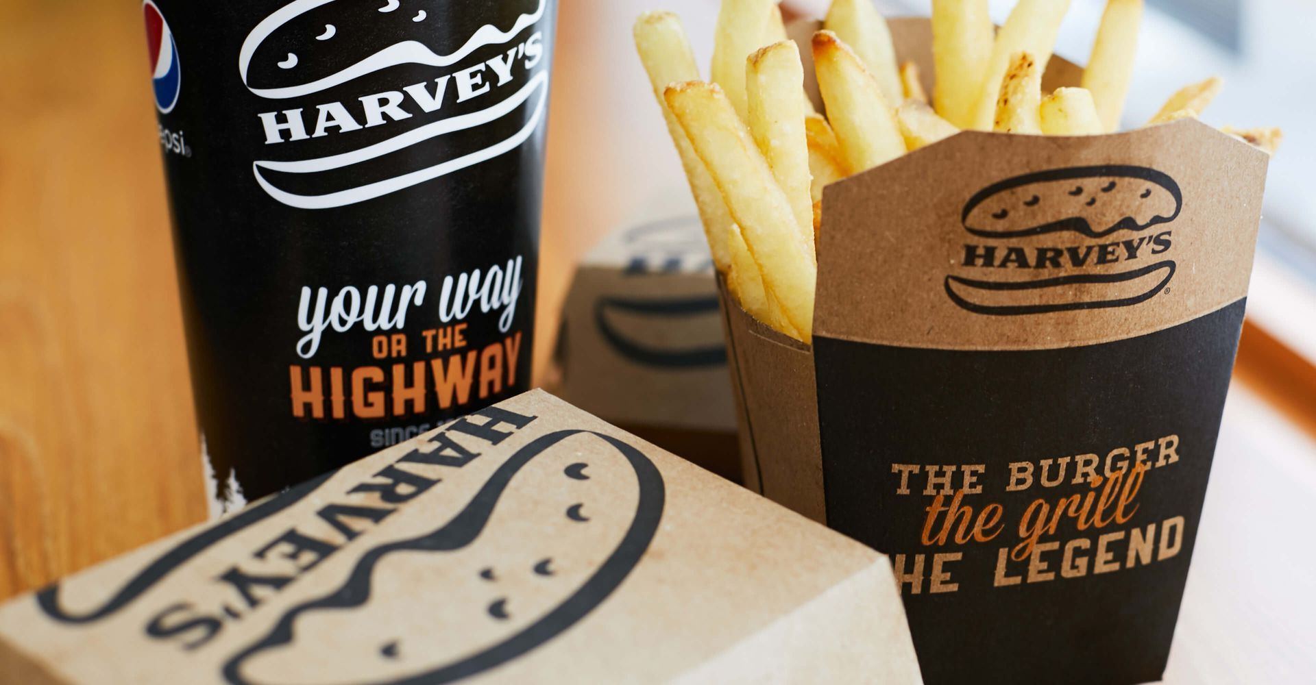 A cup of pepsi , a box of french fries and a box of hamburgers are on a table.