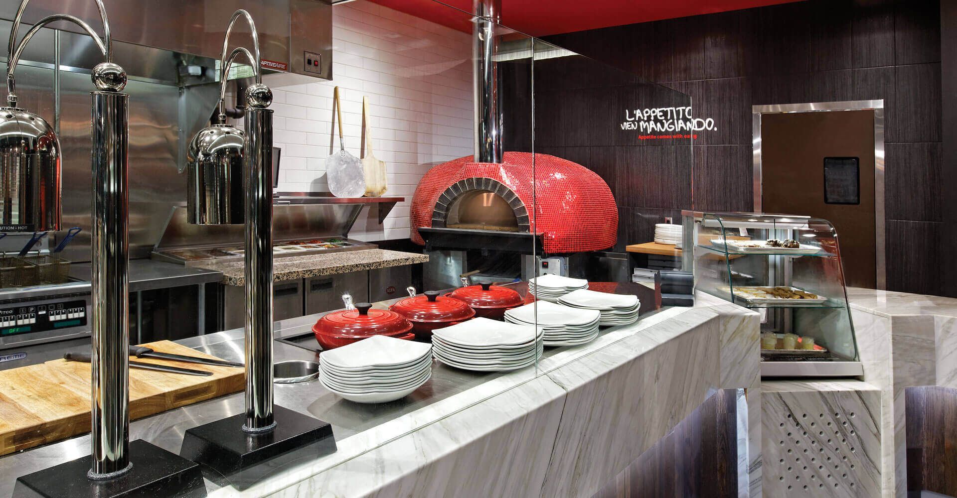 A kitchen with a red pizza oven and plates on the counter