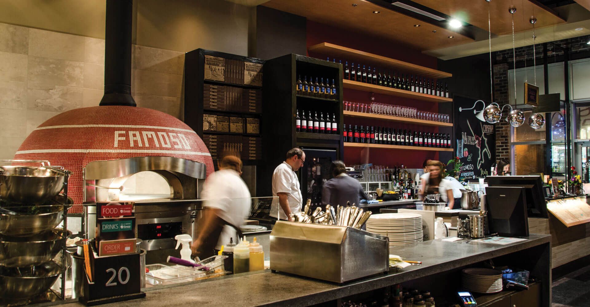 A group of people are standing around a pizza oven in a restaurant.