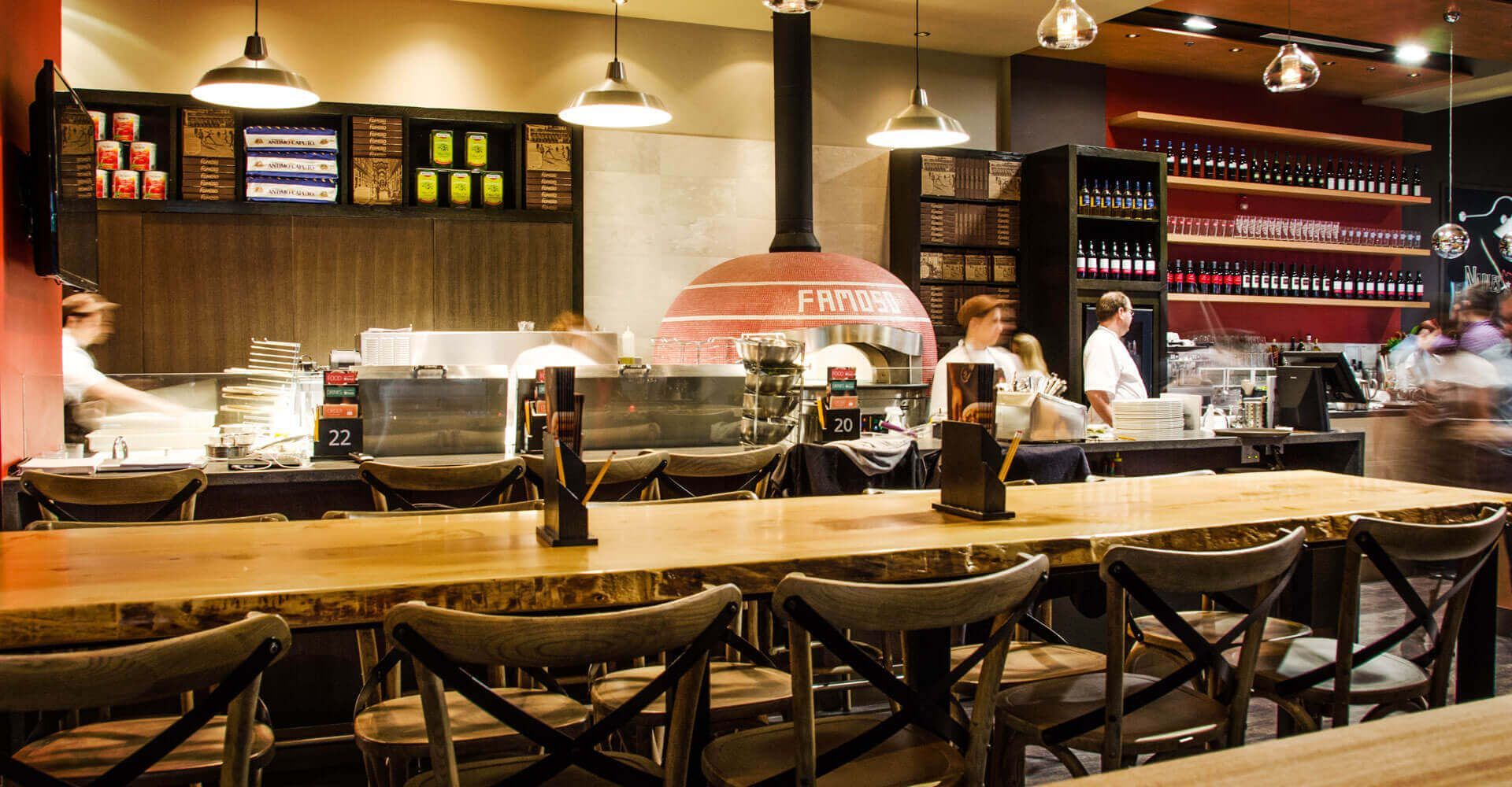 A restaurant with a long wooden table and chairs and a pizza oven.