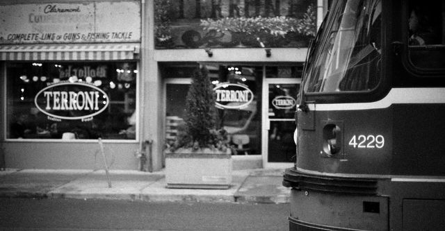 A black and white photo of a bus parked in front of a store.