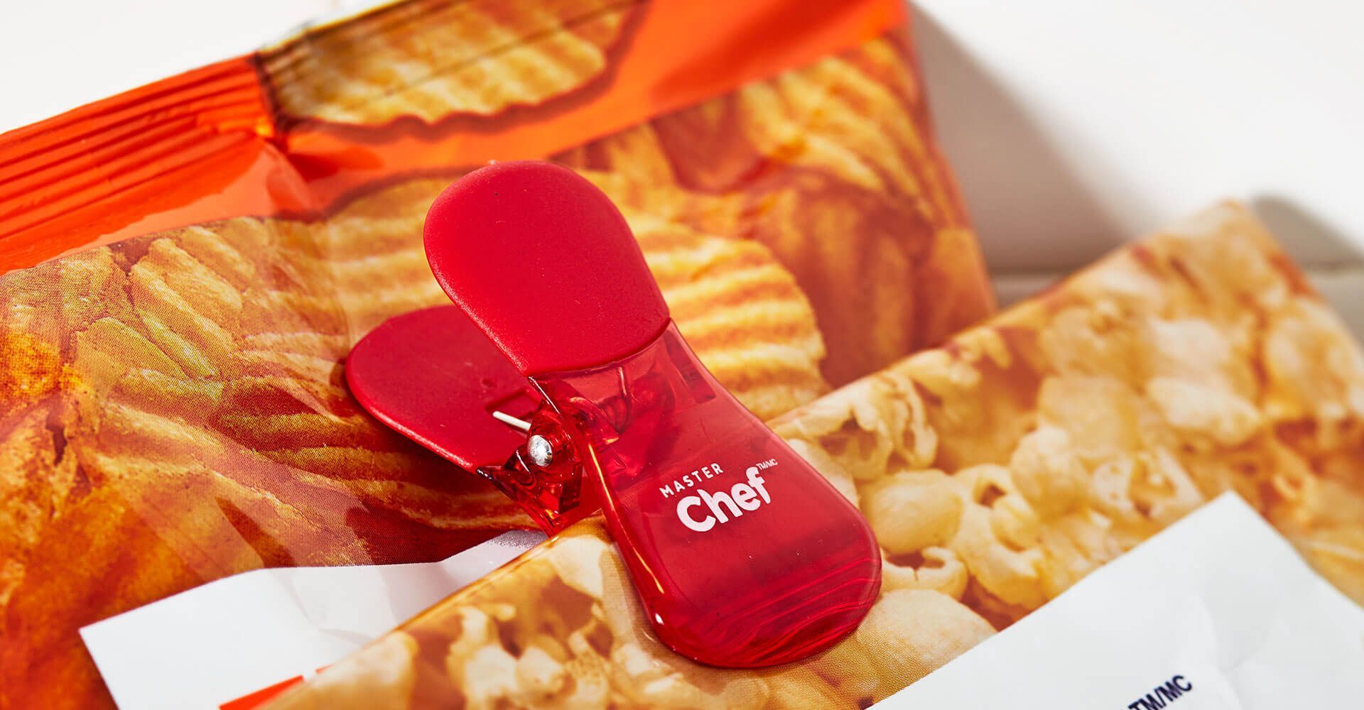 A red clip is sitting on top of a bag of chips.