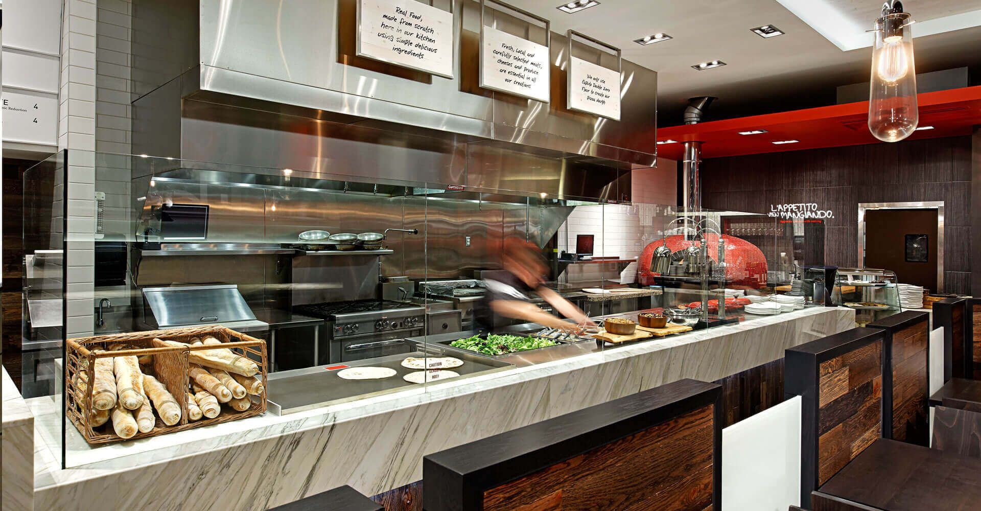 A chef is preparing food in a restaurant kitchen behind a glass counter.