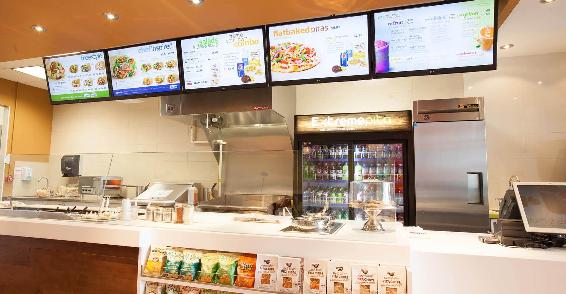 The inside of a fast food restaurant with a refrigerator and a counter.