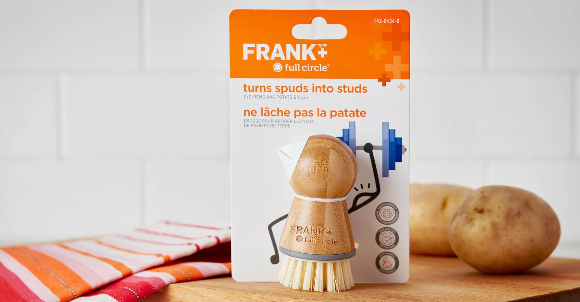 A brush is sitting on a cutting board next to potatoes.
