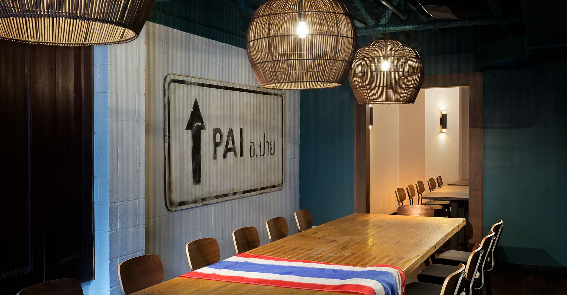 A long wooden table in a room with a sign on the wall that says pai