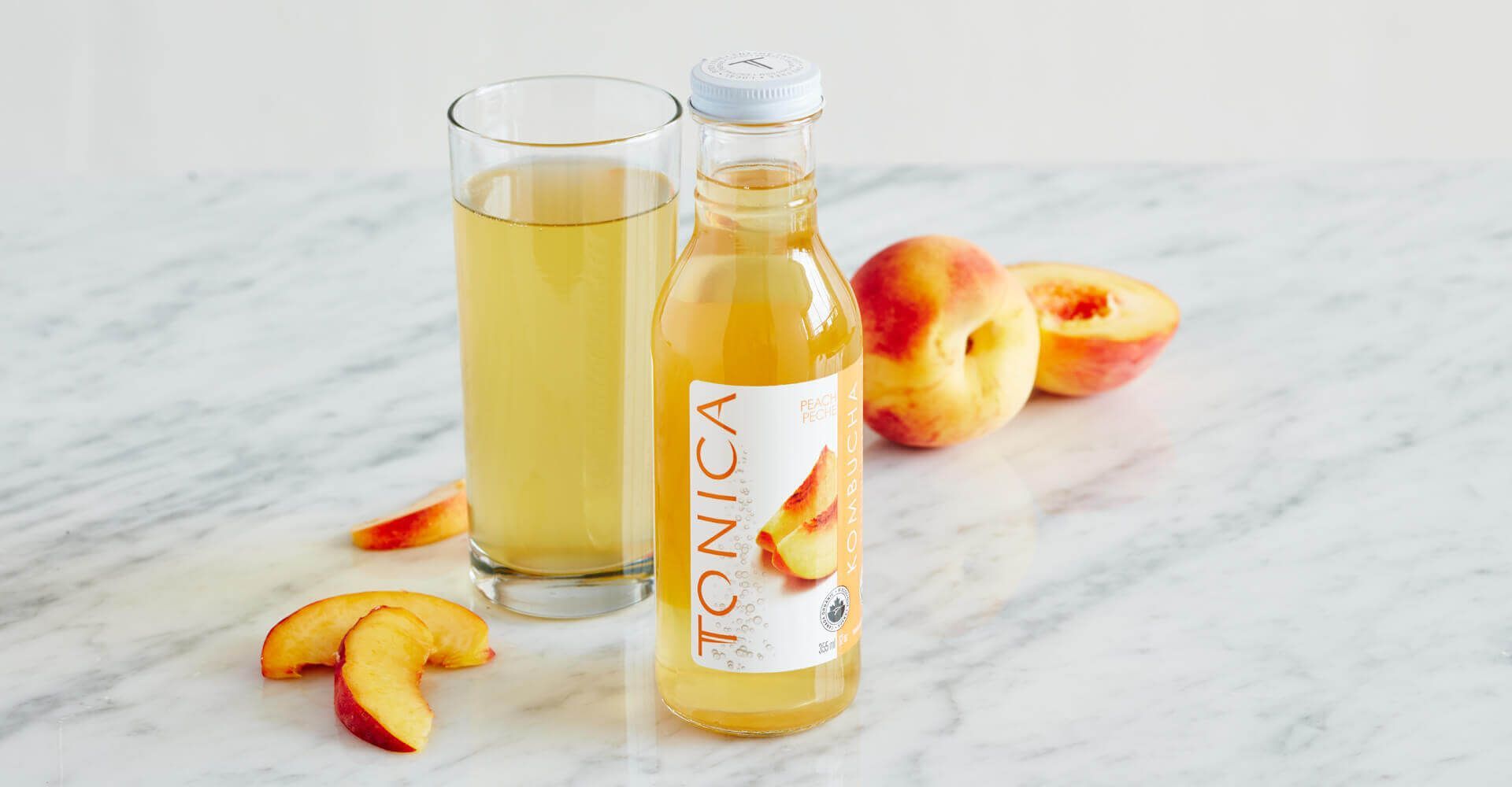 A bottle of peach juice next to a glass of peach juice on a table.
