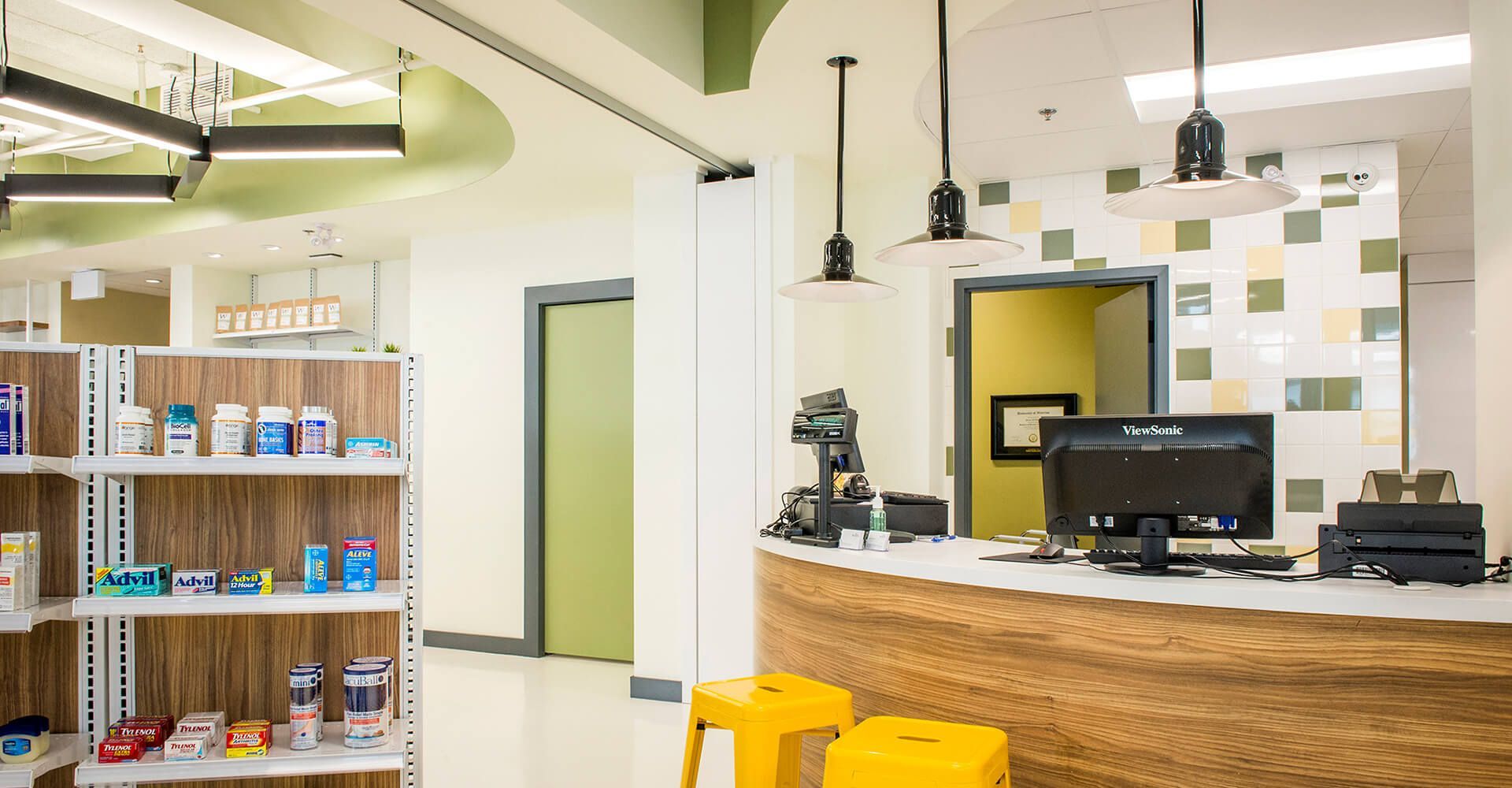A pharmacy with a counter , stools , shelves and a computer.