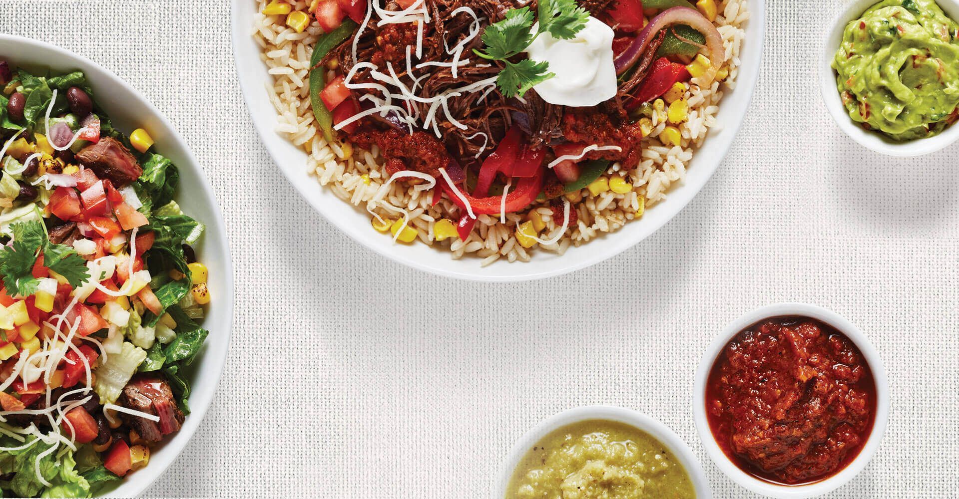A table topped with bowls of food including guacamole and salsa.