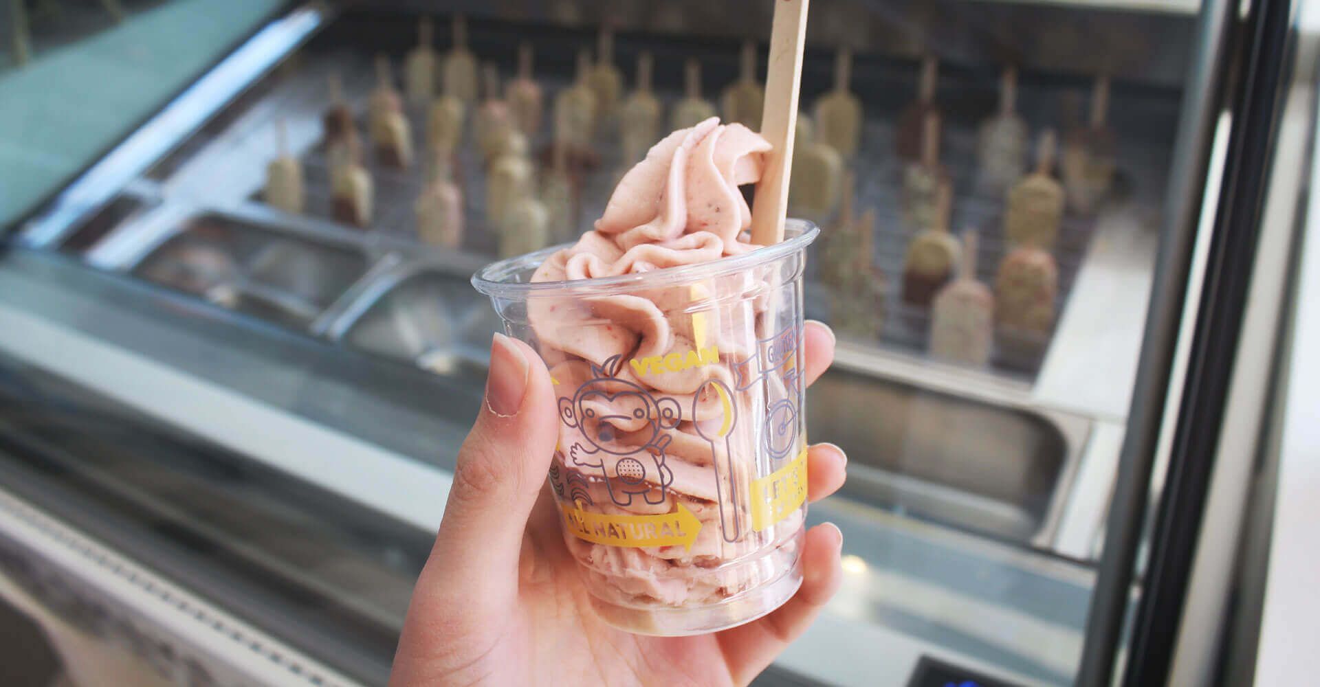 A person is holding a cup of ice cream in front of an ice cream display case.