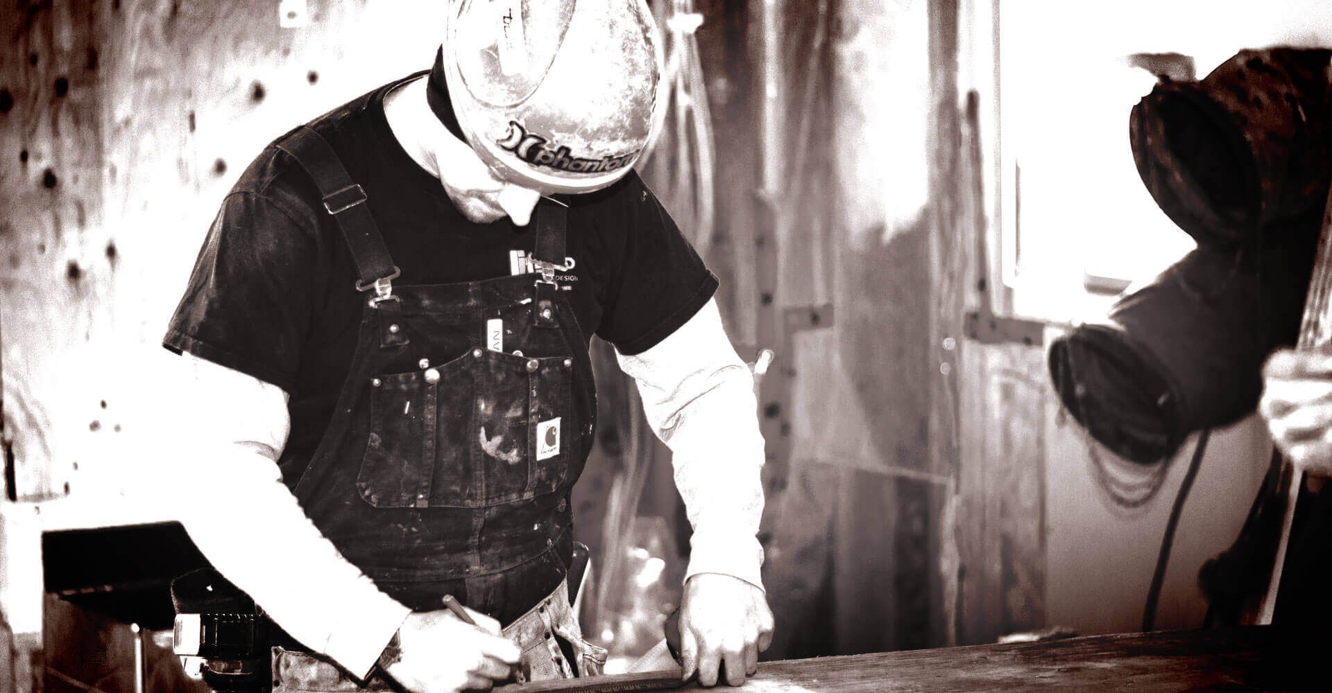 A man wearing a hard hat is working on a piece of metal.