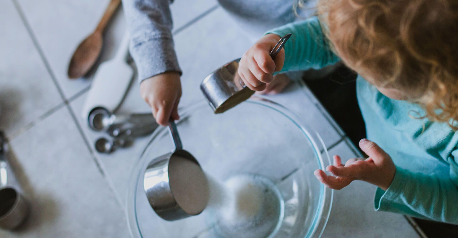 A little girl is measuring ingredients in a bowl.