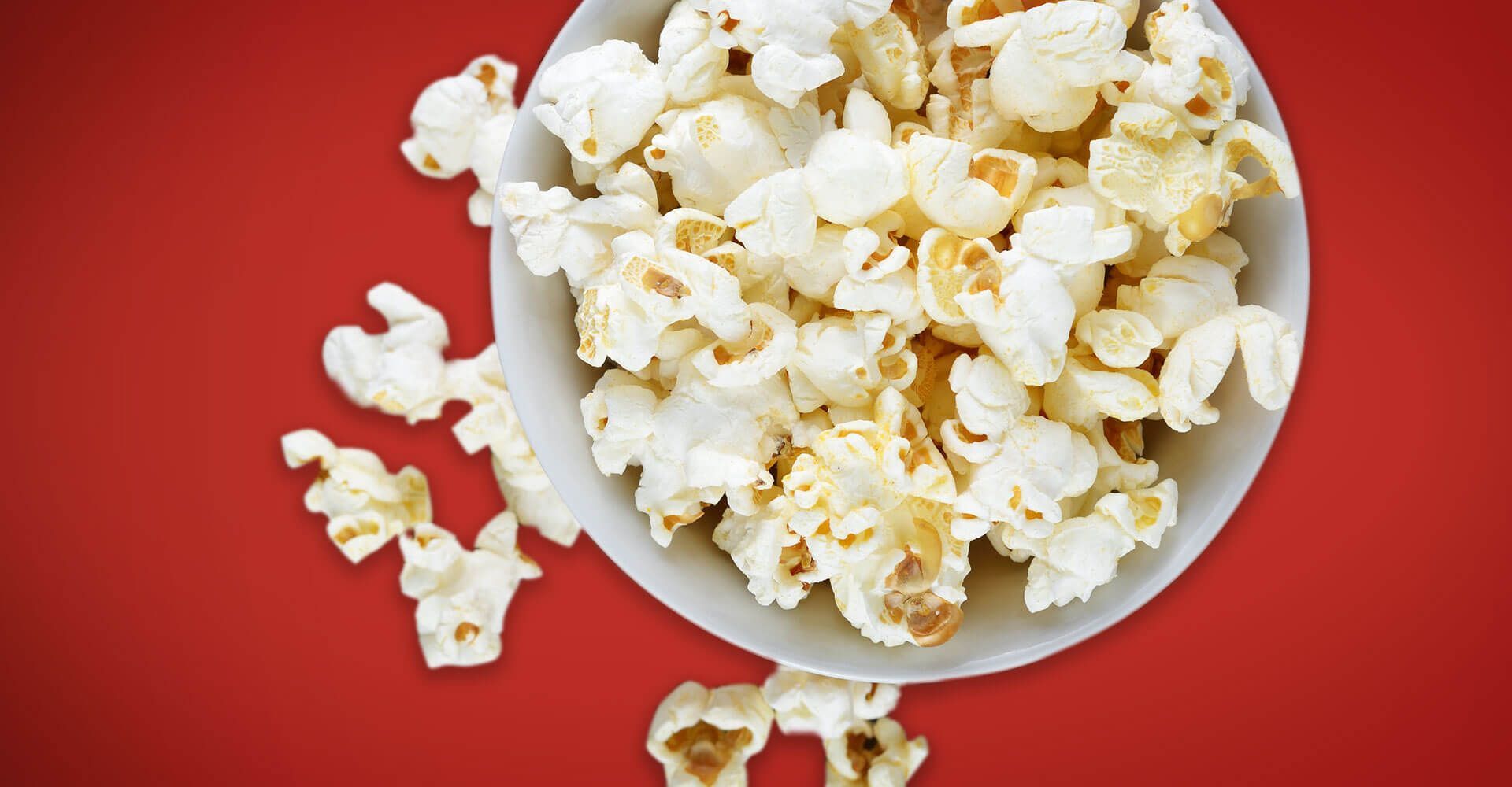 A bowl of popcorn is sitting on a red table.