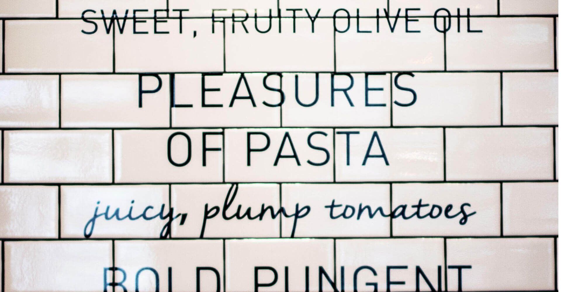 A brick wall with the words sweet fruity olive oil pleasures of pasta juicy plump tomatoes bold pungent written on it