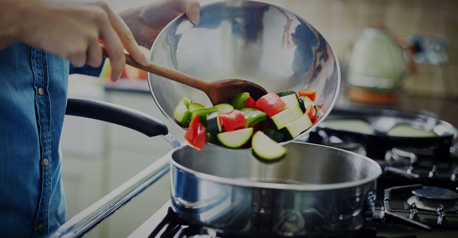 A person is pouring vegetables into a pot on a stove.