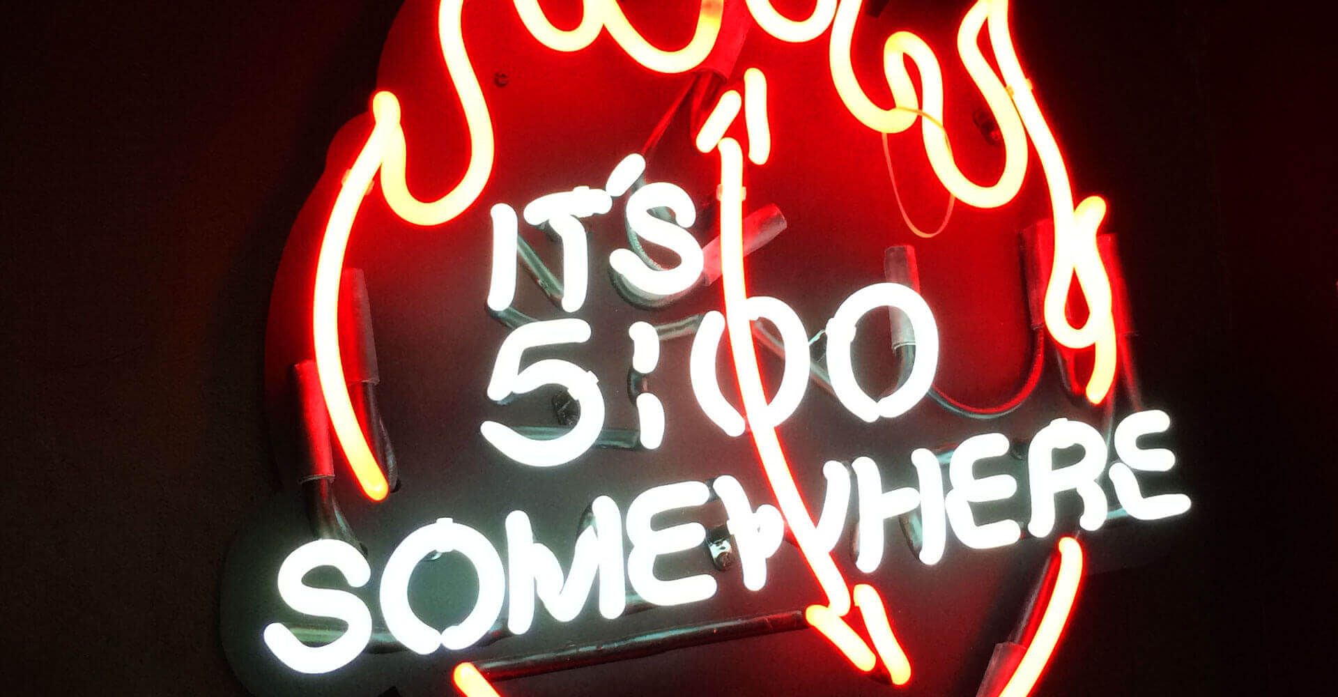 A neon sign that says it 's 5:00 somewhere