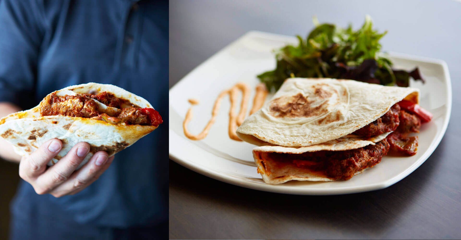 A person is holding a tortilla next to a plate of food.