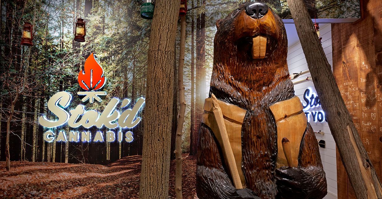 A statue of a beaver holding a stick in front of a sign.