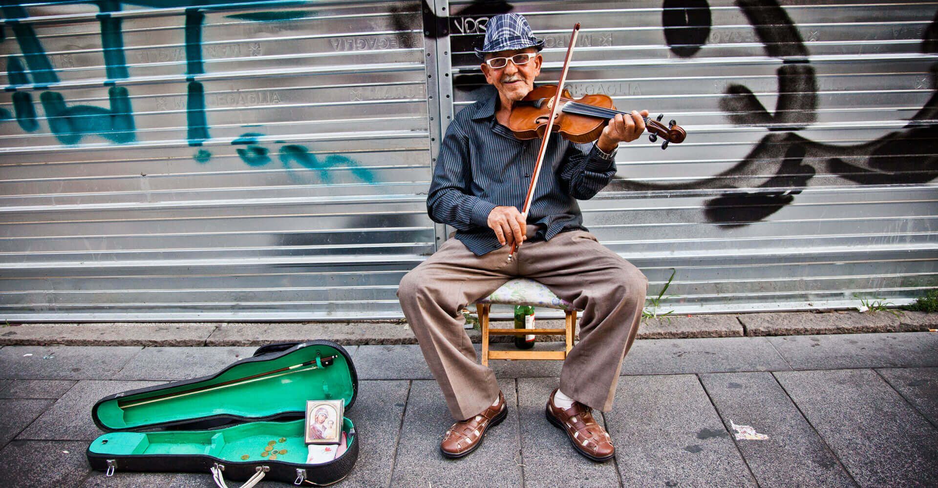 A man is sitting on the sidewalk playing a violin.