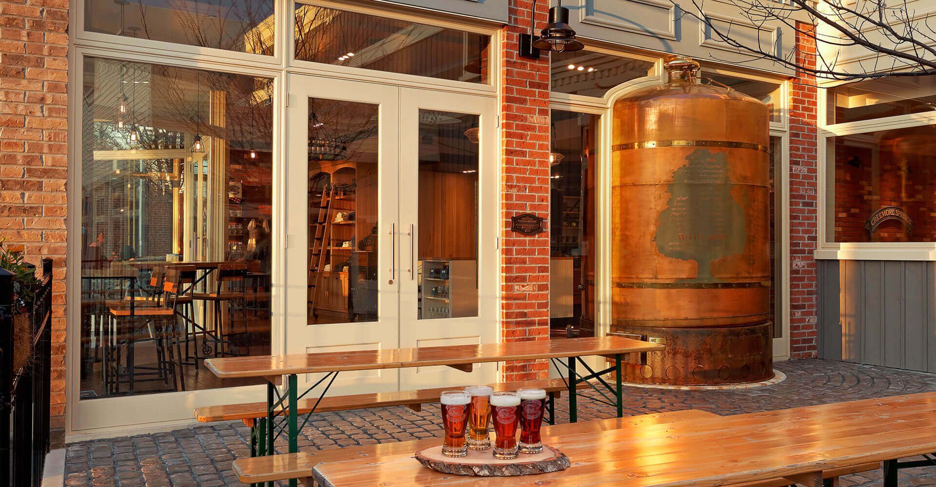 A table with three glasses of beer on it in front of a brick building.