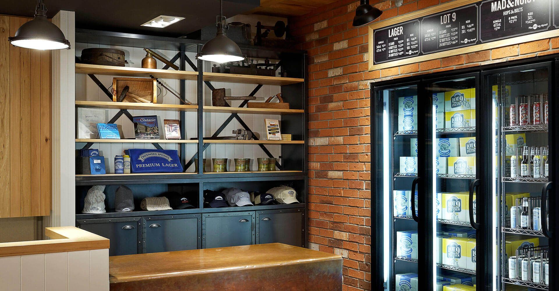 A restaurant with a brick wall , a counter , and a refrigerator filled with beer.