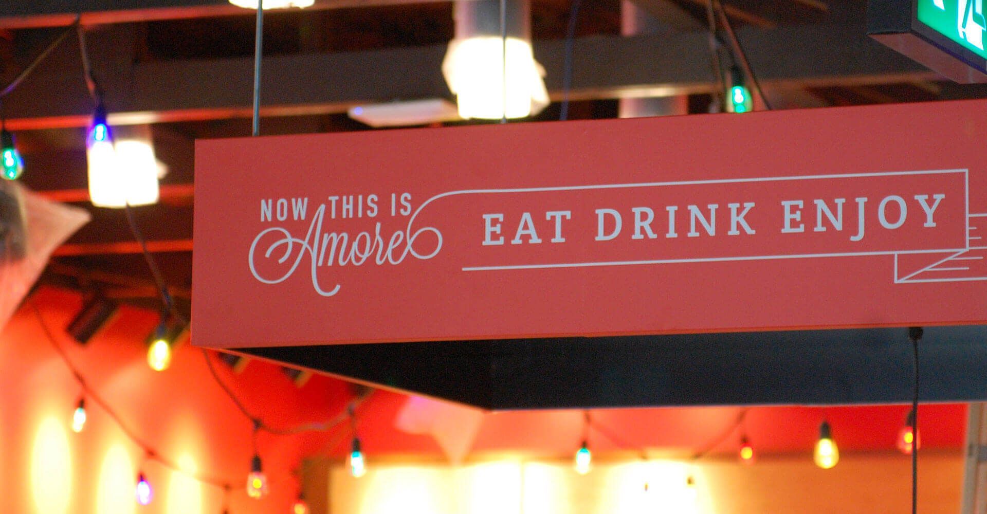 A sign that says now this is amore eat drink enjoy