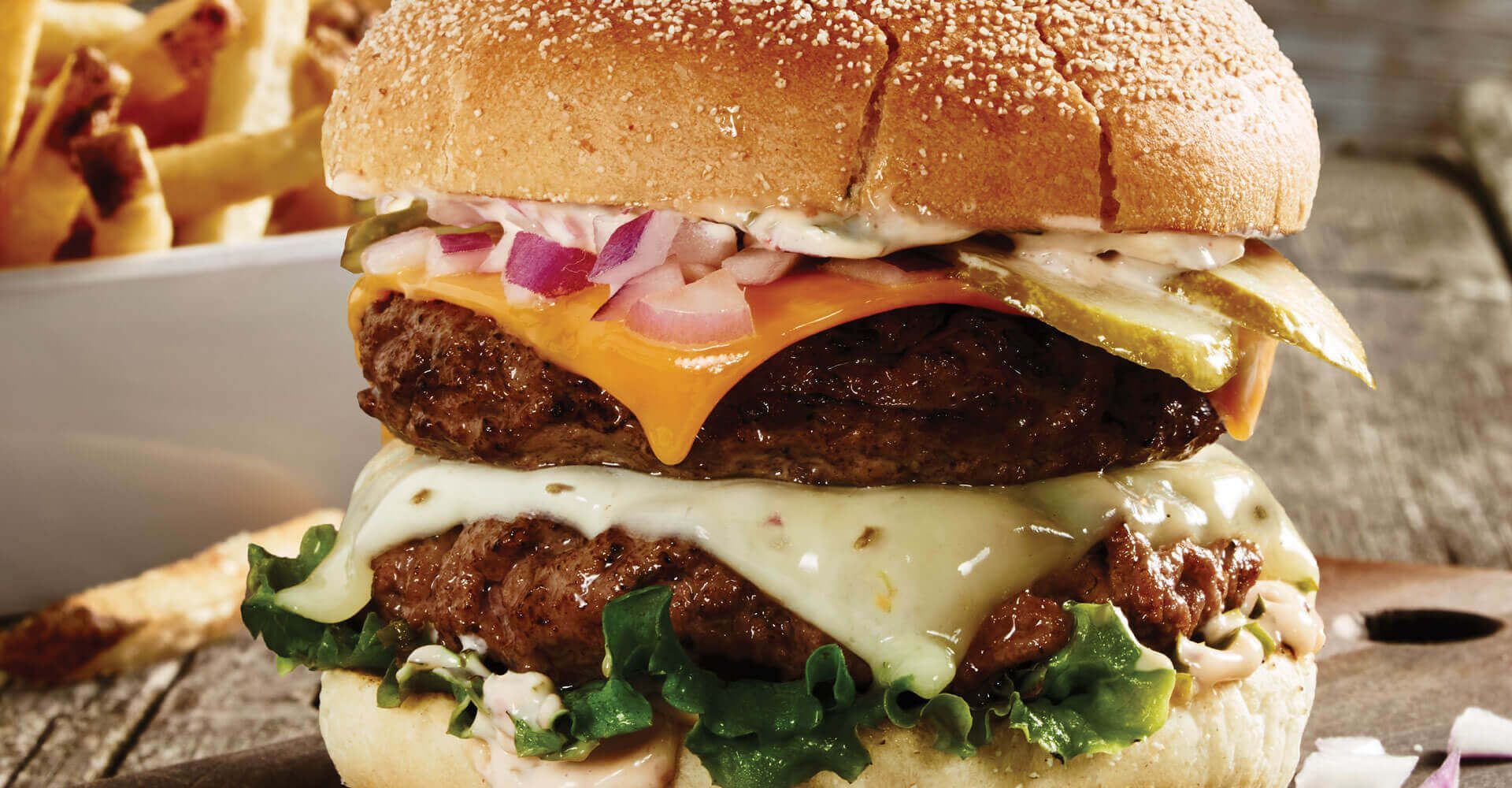 A hamburger is sitting on a wooden table next to a bowl of french fries.