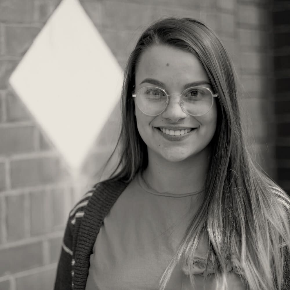 A woman wearing glasses is smiling in a black and white photo.