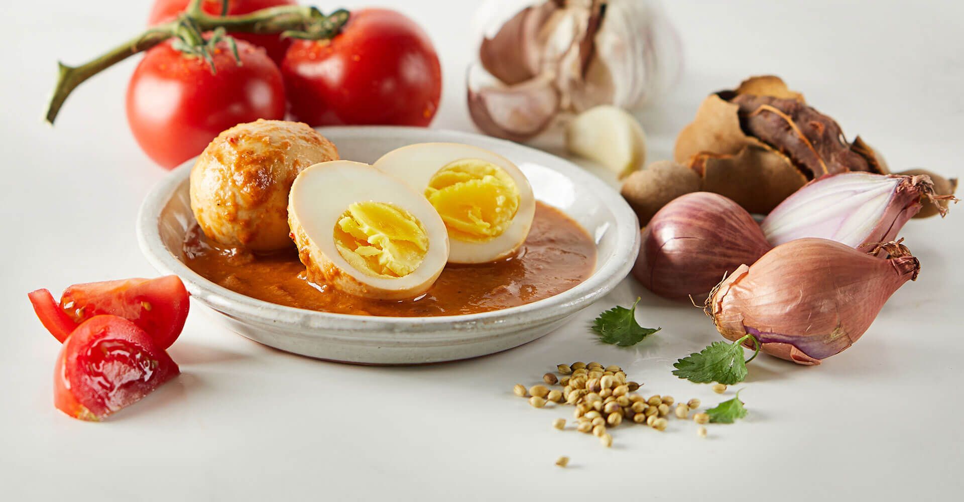 A bowl of hard boiled eggs surrounded by vegetables on a table.