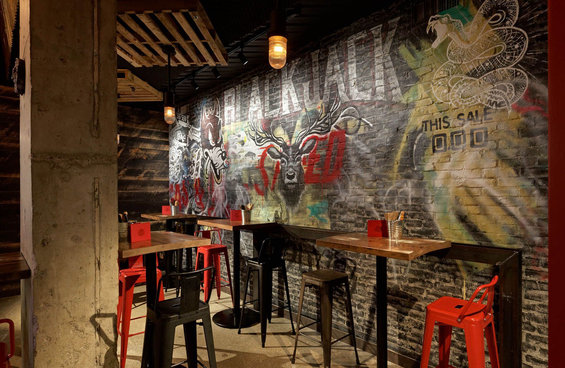 A restaurant with tables and chairs in front of a brick wall with graffiti on it.